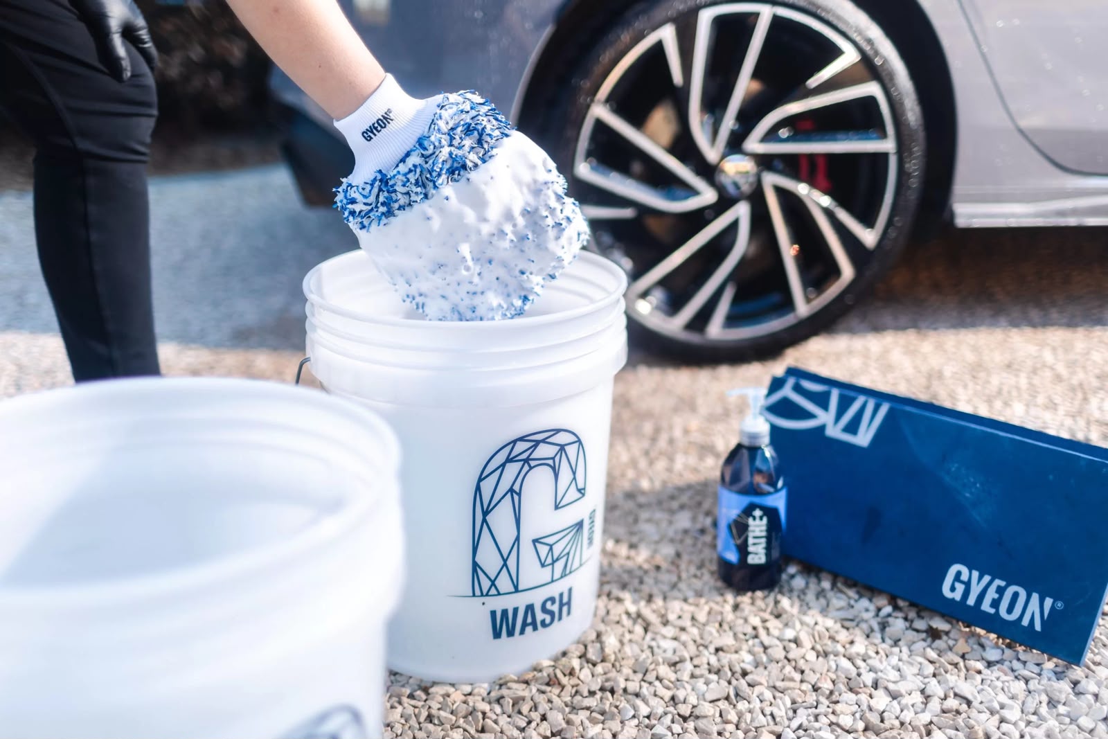 Seau GYEON WASH avec gant microfibre et produit GYEON Bathe+ devant la roue d'un véhicule